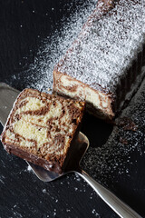 Homemade chocolate marble cake on a slate cutting board covered with icing sugar. Piece cut with a cake slicer