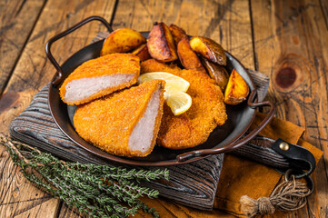 Delicious crispy pork schnitzel with fried potato wedges. Wooden background. Top view