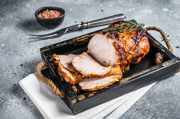 Glazed roast pork roll in wooden tray with herbs. Gray background. Top view