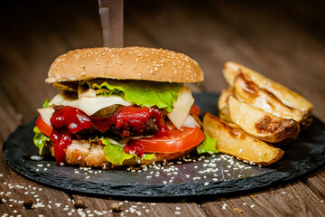 Closeup hamburger with french fries, ketchup, and fresh vegetables on stone board. Homemade cooking