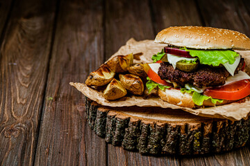 Front view of beef burger with baked potatoes on rustic wooden serving table. Selective focus 
