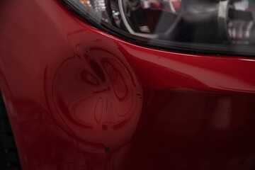 Dent on the bumper of a red car for repair in a paint shop