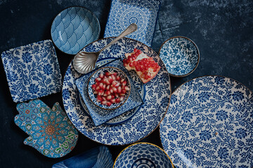 Red ripe pomegranate seeds, pieces with skin and membranes of cuted fruit on glazed ceramic blue...