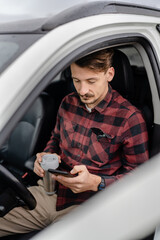 man hold cup with coffee use mobile phone sit in the car take a brake