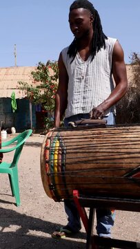 Vertical video of Wide shot of black man playing dundun with wooden stick