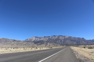 Asphalt Road Journey Through The Mountains In The Desert With Sand And Blue Skies In The Distance