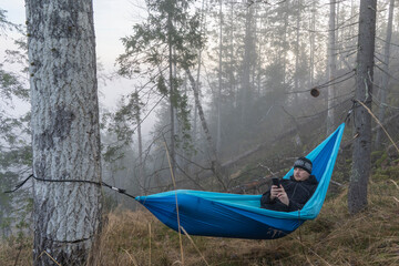 Man wit phone in the hammock in the forest.