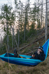 A young man in a hammock drinks coffee and eats cookies.