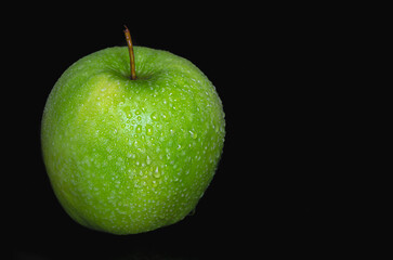 Green apple in water drops on a black background isolated.