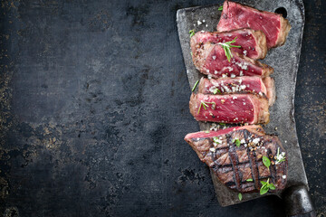 Traditional barbecue wagyu sirloin beef steak served sliced with salt and herbs on a rustic kitchen...