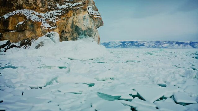 Lake Baikal, flying over broken ice, blue snow hummocks. Ridge of mountains and yellow rock in the background. A beautiful winter landscape. Baikal, Siberia, Russia. Drone aerial shot 4k