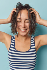 Positive Asian woman poses with wet hair after taking shower feels fresh smiles toothily has eyes...