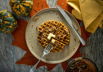 Overhead photo of a paleo pumpkin waffle with orange autumn table setting. - 557776086
