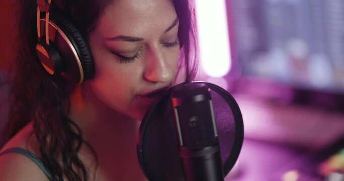 Female music producer in studio with audio recording equipment. Girl singing on a professional studio microphone. Close up abstract video.