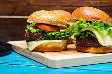 Homemade hamburgers with meat, cheese, lettuce, tomato on a wooden table