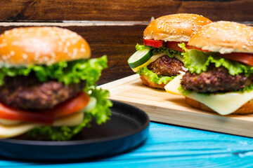 Homemade hamburgers with meat, cheese, lettuce, tomato on a wooden table
