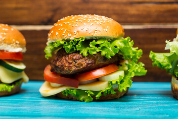 Homemade hamburgers with meat, cheese, lettuce, tomato on a wooden table