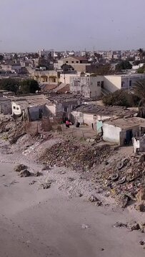 Vertical video of Slums built along sandy beach, city buildings in background