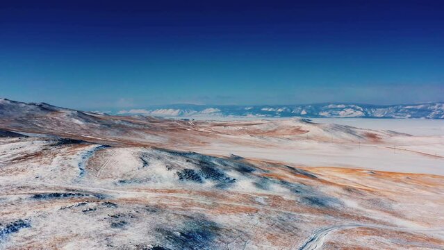 An alien landscape in the valley of Oykhon Island on Lake Baikal. Red earth sprinkled with snow. Winter on Mars. Blue sky. Baikal, Siberia, Russia. Drone shooting 4k