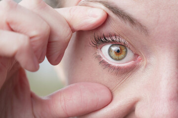 Close up view of a girl's tan eye. Woman spreads her eyelids with her fingers, opening her eye...