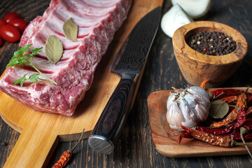Raw ribs with peppercorns, bay leaves and spices on a cutting board. On a black background.