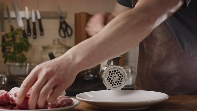 Home chef preparing a BBQ recipe - the Balkan kebapche or cevapcici. Mincing meat on a manual mincing machine at home. Closeup shot. Low angle.