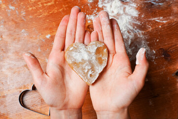 Childs hands holding biscuit cookie as heart out of dough. Heart molds and flour on a table....
