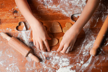 Hands of child makes biscuits cookies as hearts out of dough. Heart molds, rolling pin and flour on...