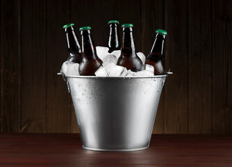 Metal bucket with bottles of beer and ice cubes on wooden table - obrazy, fototapety, plakaty