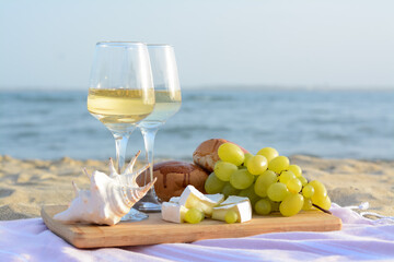 Glasses with white wine and snacks for beach picnic on sandy seashore