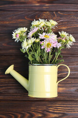 Watering can with flowers on wooden table, top view
