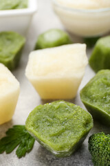 Frozen cauliflower and broccoli puree cubes on light grey table, closeup