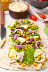 Tortilla with hummus and vegetables on table, closeup