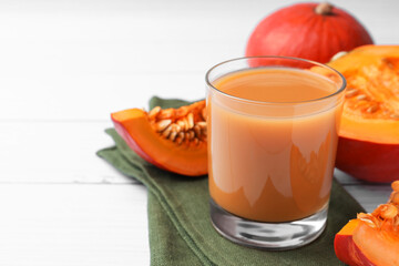 Tasty pumpkin juice in glass, whole and cut pumpkins on white wooden table. Space for text