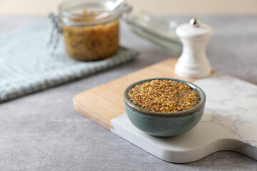 Wooden board with bowl of delicious whole grain mustard on grey table, space for text