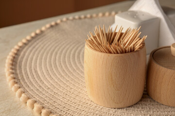 Wooden holder with many toothpicks on wicker mat, closeup. Space for text