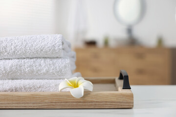 Wooden tray with stacked bath towels and beautiful flower on white table indoors. Space for text