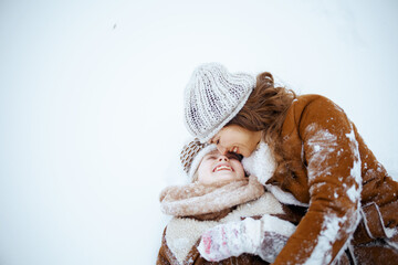 happy modern mother and daughter laying in snow