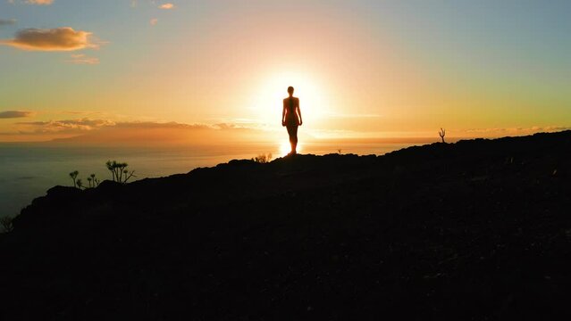 Lonely woman silhouette on mountain top with ocean view at sunset. Aerial Tenerife Island. Sunburst rays otline a person. Alone girl enjoying sunrise. Sunbeams rise from sea.