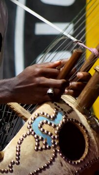 Vertical video of Black man dancing while his fingers are plucking the strings of kora instrument