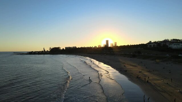 Atardecer en playa donde el sol se encuentra detras de edificios de ciudad 