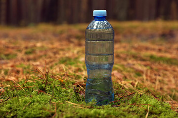 Plastic bottle of fresh water on ground in forest