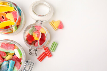 Tasty jelly candies in jars on white table, flat lay. Space for text