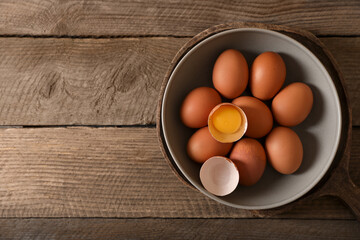 Bowl with raw chicken eggs on wooden table, top view. Space for text