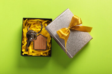 Key with trinket in shape of house and gift box on light green background, flat lay. Housewarming party