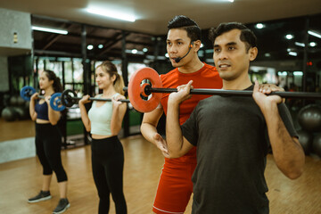 male instructor with microphone correcting barbell lifting positions to young men during group exercises in fitness center
