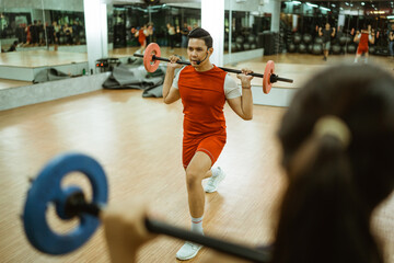 an instructor in a red shirt lifts barbell back squat in front of a woman during a body combat...