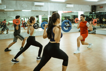 the male instructor set an example for the sporty group doing barbell back squats at the fitness...