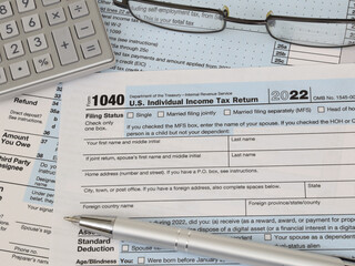 An IRS 1040 tax year 2022 form is shown in 2023, along with an ink pen, calculator, and glasses. The Internal Revenue Service tax filing deadline is April 18 this year.
