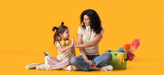 Mother and daughter with cleaning supplies giving each other high-five on yellow background